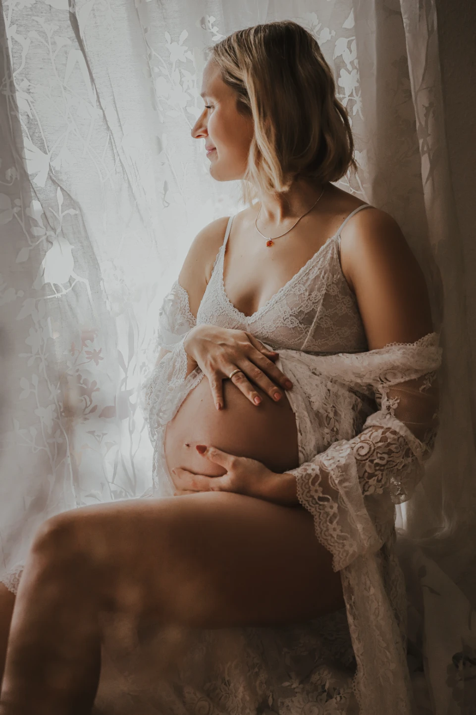 A stylish image of a pregnant women looking out a window in natural lighting inside a room